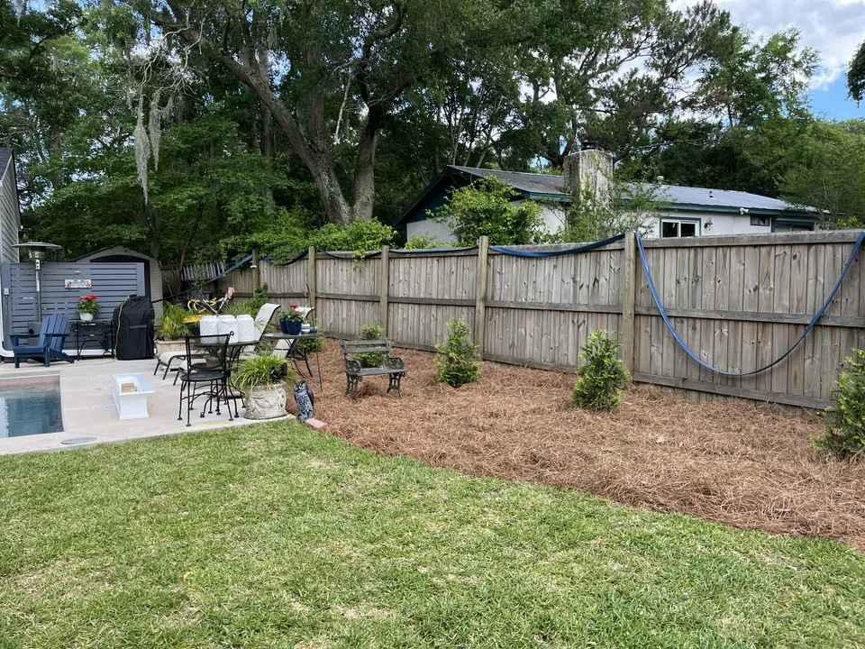 Lawn bordered by trees and mulched beds near an outdoor seating area