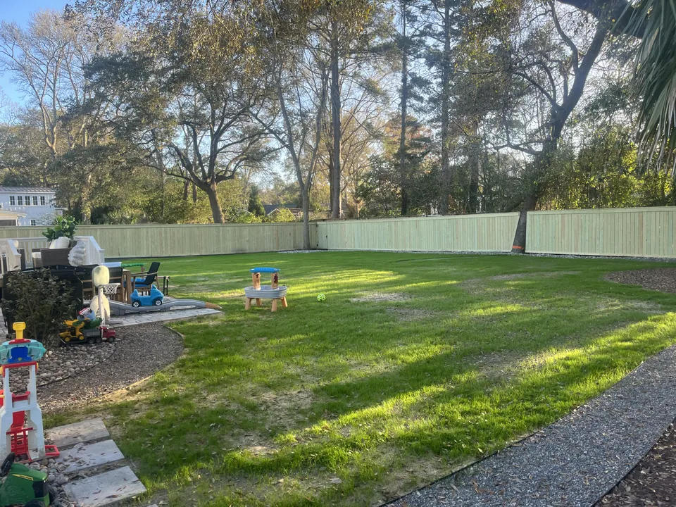 Wide view of the lawn and garden edge beside a fenced backyard